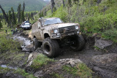 2003 Jeep TJ - Several off-road vehicles traverse a challenging, muddy mountain path during an outdoor event.