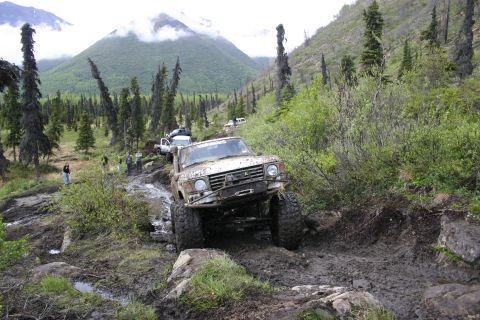 2003 Jeep TJ - Several off-road vehicles traverse a challenging muddy and rocky path through a wooded mountain landscape.