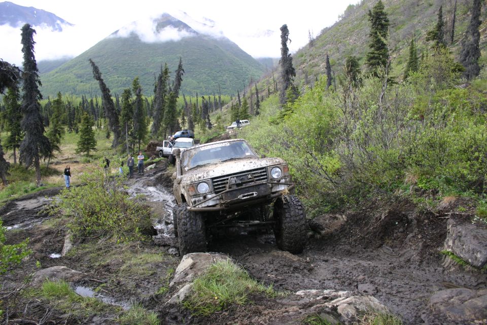 Muddy off-road vehicle on a steep, rocky trail with trees and mountains in background