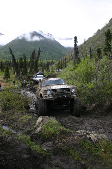 2003 Jeep TJ - Off-road vehicles tackle a challenging muddy and rocky trail in a mountainous, forested area.