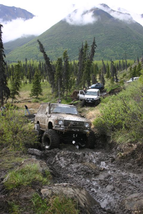 2003 Jeep TJ - Several off-road vehicles tackle a challenging, muddy path through a wooded, mountainous area.
