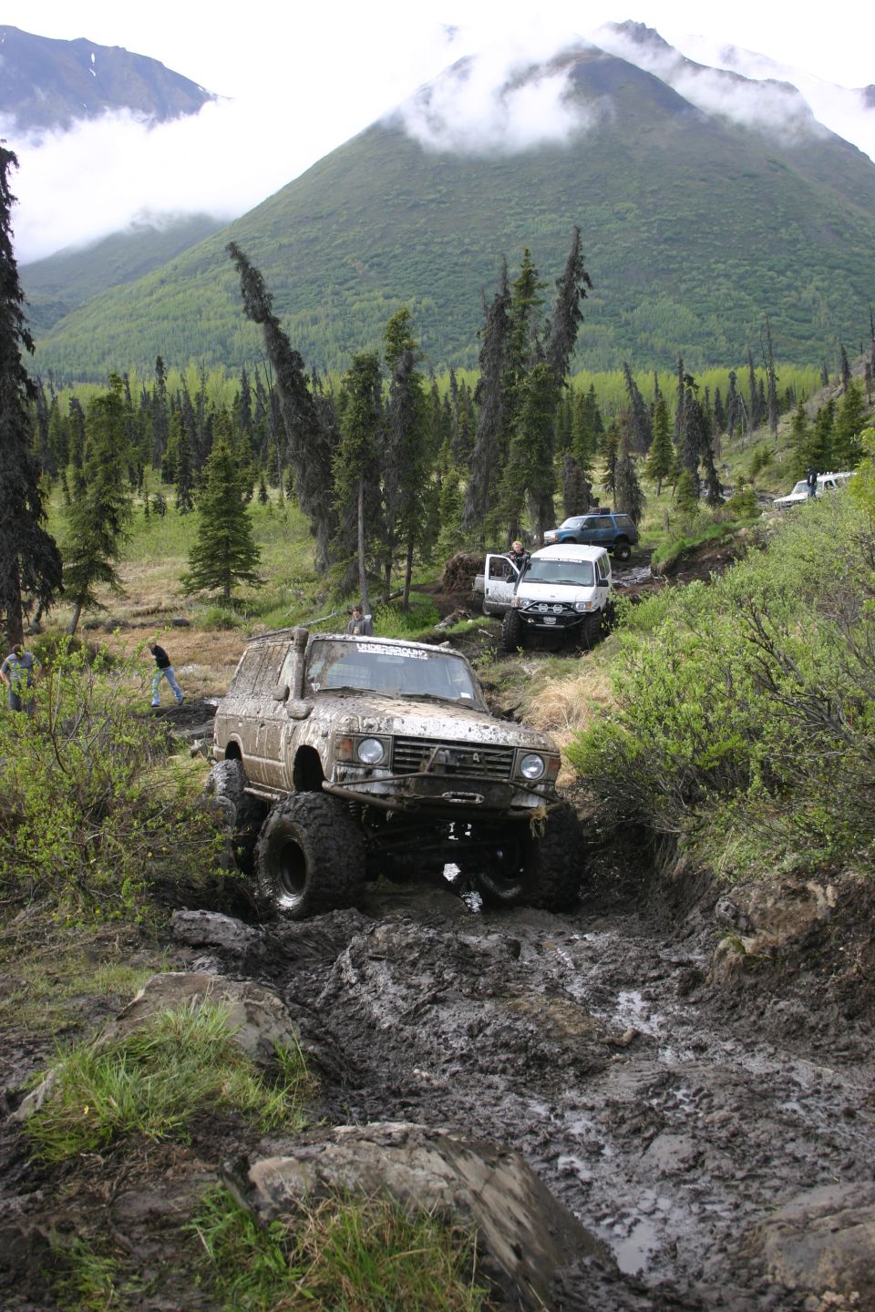 Muddy off-road vehicle navigating a difficult trail with other vehicles behind it