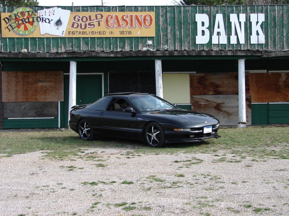 Black Ford Probe coupe parked in front of an old wooden Gold Dust Casino and Bank building