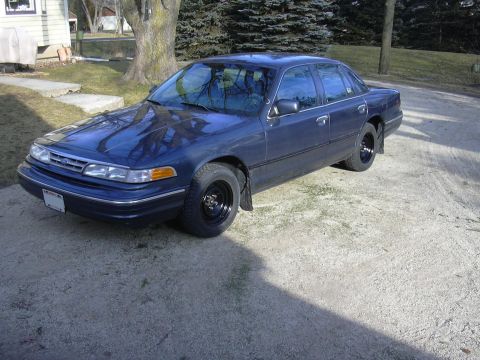 1996 Ford Crown Victoria - A dark blue sedan is parked outside a house on a sunny day, showing its front three-quarter view.