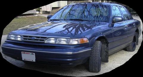 1996 Ford Crown Victoria - This blue sedan features a prominent Ford emblem on its grille and is equipped with aggressive off-road tires.