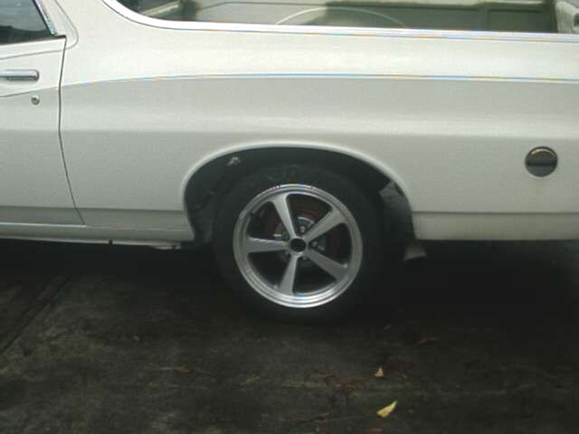 White car's rear quarter panel and five-spoke polished alloy wheel with blackwall tire