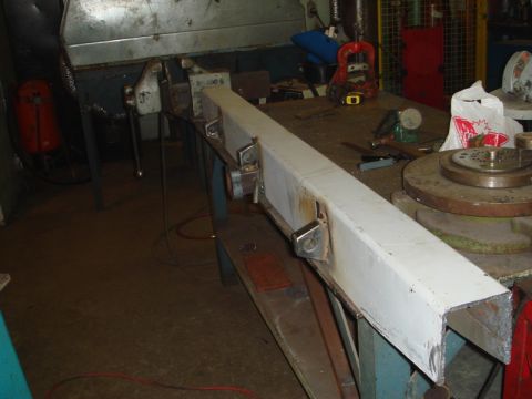 1996 Ford Bronco - A white metal bumper part is secured in a vise on a workbench in a workshop.