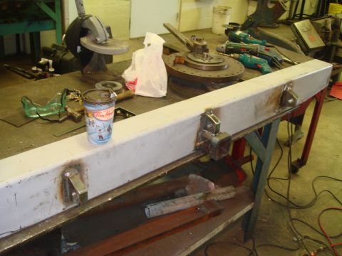 1996 Ford Bronco - A metal bumper part, likely for a vehicle, is shown on a workbench with various tools and a beverage cup.
