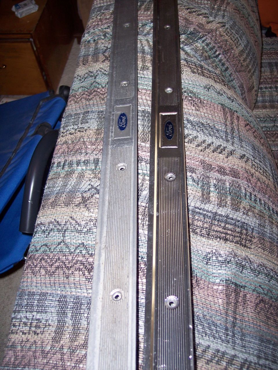 Two ribbed aluminum Ford door sill scuff plates with blue oval badges, one dull one polished