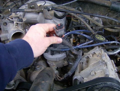 1990 Ford Bronco - Close-up of an engine bay, focusing on a hand disconnecting a wire harness.