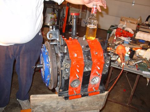 1986 Mazda RX-7 - A person is working on a rotary engine, with a beer bottle precariously balanced on top.