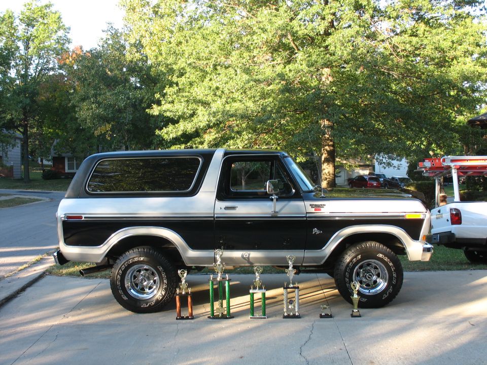 Side view of black and silver Ford Bronco in driveway with seven trophies displayed in front