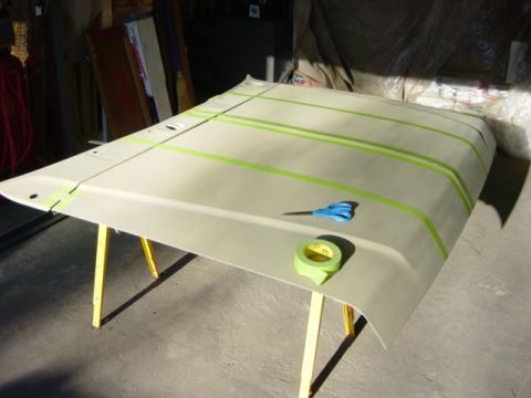 1991 Ford Bronco - A vehicle hood is prepped for painting with masking tape and scissors on sawhorses in a workshop.