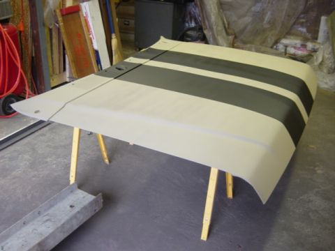1991 Ford Bronco - A car hood with dark racing stripes is shown on sawhorses in a workshop.