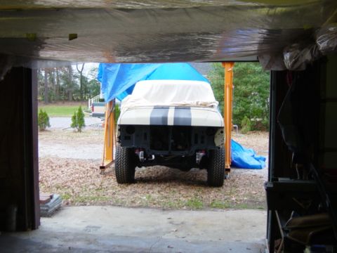 1991 Ford Bronco - Vehicle covered with a tarp and sheet, showing its front end with black stripes on the hood, parked outdoors.