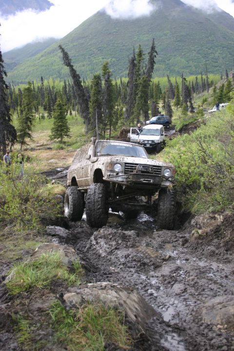 2003 Jeep TJ - Multiple off-road vehicles tackle a challenging muddy trail in a mountainous, wooded area.