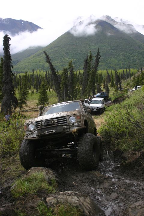 2003 Jeep TJ - Several off-road vehicles traverse a challenging muddy path in a mountainous, forested area.