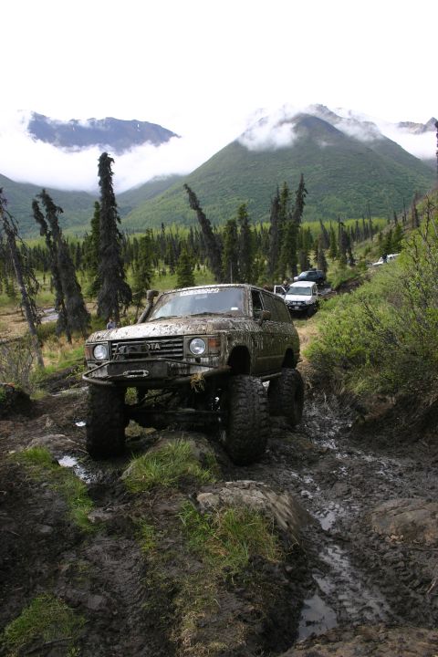 2003 Jeep TJ - A convoy of off-road vehicles navigates a challenging muddy trail in a mountainous, forested area.
