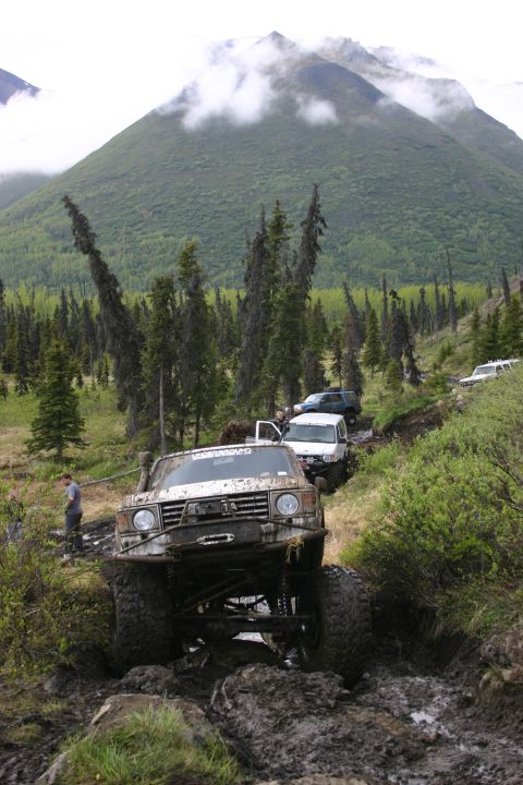 2003 Jeep TJ - Several off-road vehicles traverse a challenging muddy path through a wooded mountain landscape.