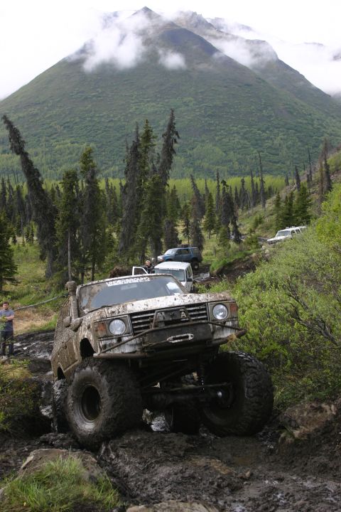 2003 Jeep TJ - Several off-road vehicles navigate a challenging muddy track in a mountainous, forested area.