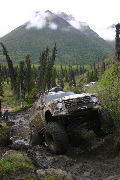 2003 Jeep TJ - Off-road vehicle struggles through a challenging muddy and rocky terrain in a mountainous area.