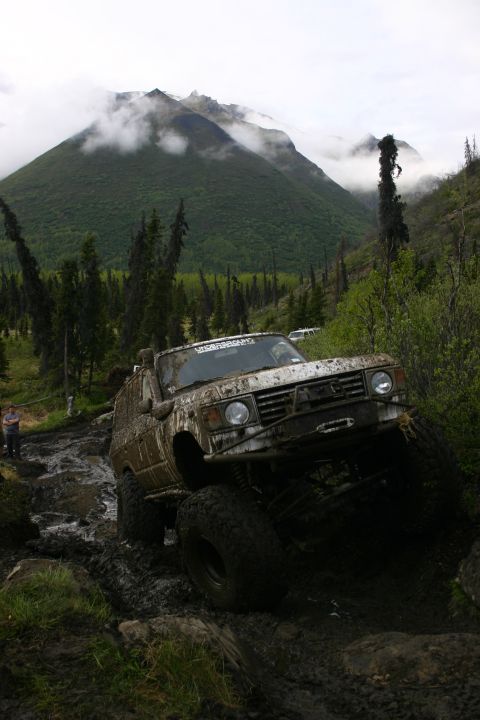 2003 Jeep TJ - An off-road vehicle tackles a challenging muddy terrain with a person observing from the side.