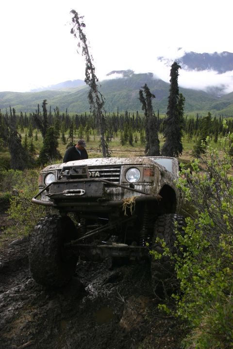 2003 Jeep TJ - A heavily modified Toyota Land Cruiser FJ60 navigates a muddy, off-road trail in Alaska.