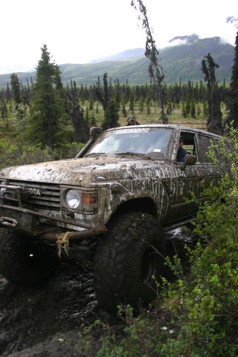 2003 Jeep TJ - Muddy 1980 Toyota Land Cruiser FJ60 navigating off-road terrain with a snorkel and large tires.