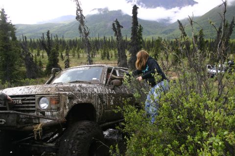 2003 Jeep TJ - A person attempts to free a mud-covered Toyota Land Cruiser from dense vegetation in a wooded, mountainous area.