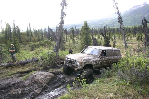 2003 Jeep TJ - An off-road SUV struggles through a muddy, wooded terrain during an outdoor event.