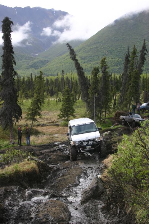 2003 Jeep TJ - Multiple off-road vehicles traverse a challenging muddy path through a forested mountain landscape.