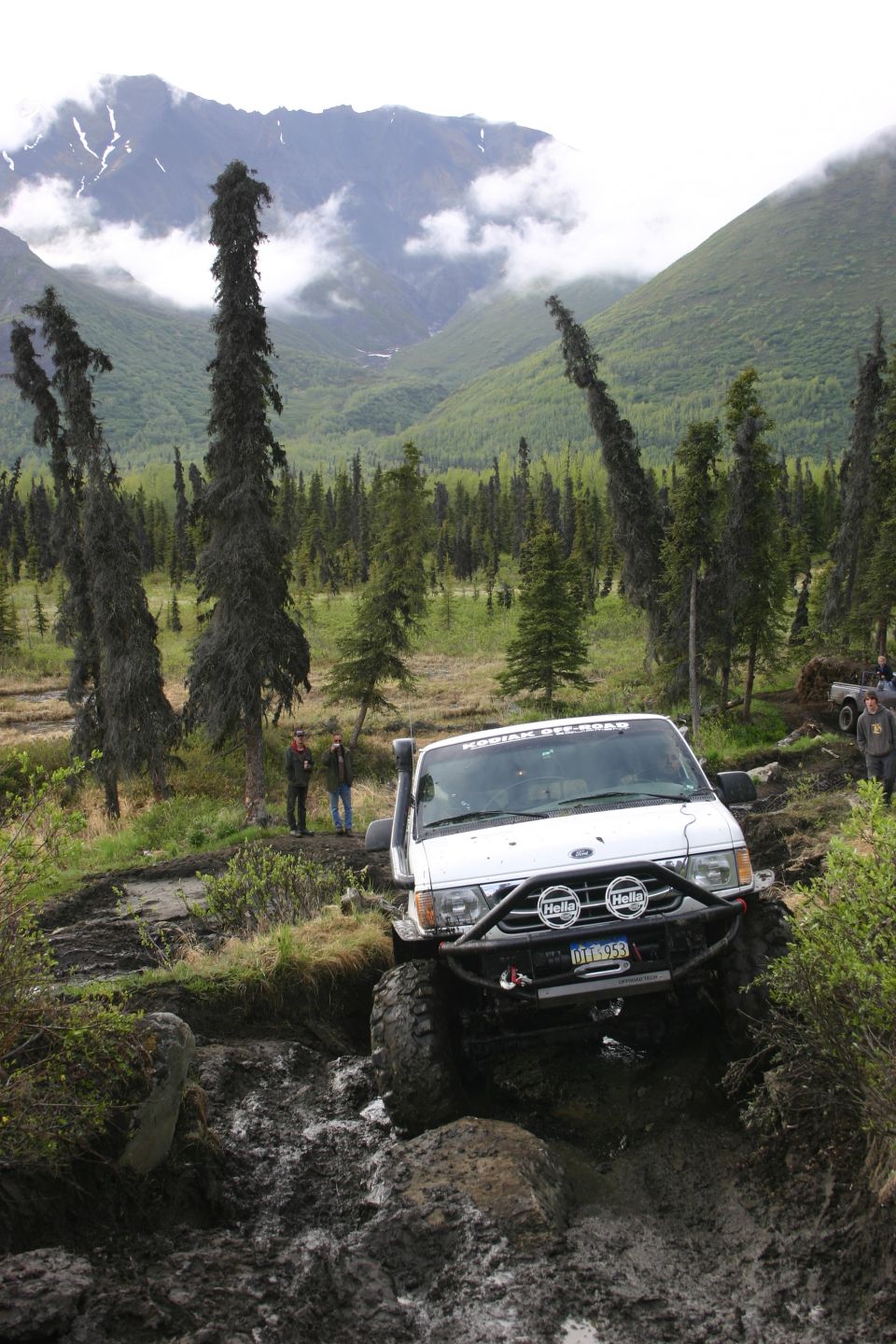 White off-road SUV with snorkel and brush guard navigating a muddy trail