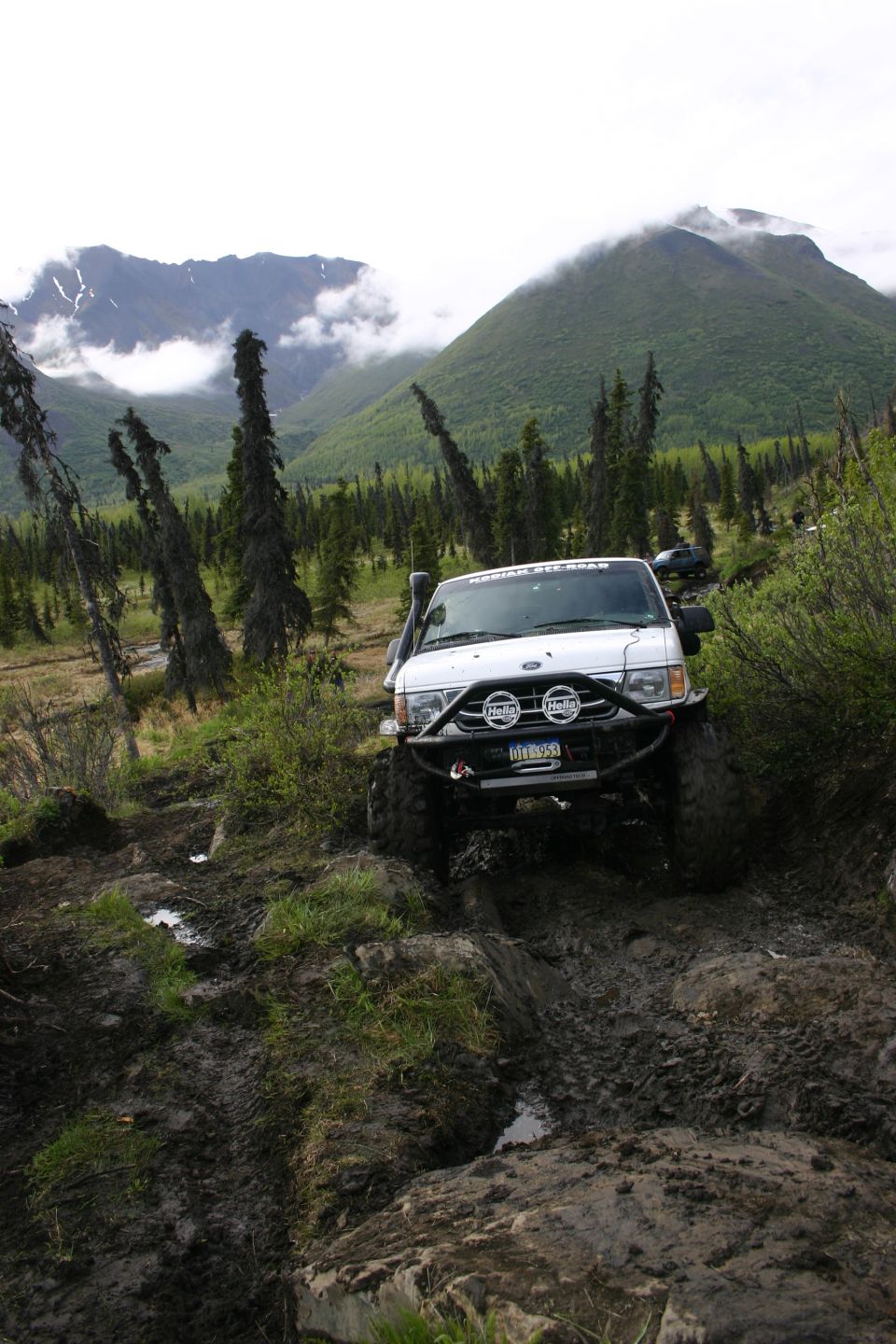 White van with snorkel and off-road bumper driving through mud and rocks, mountains in background