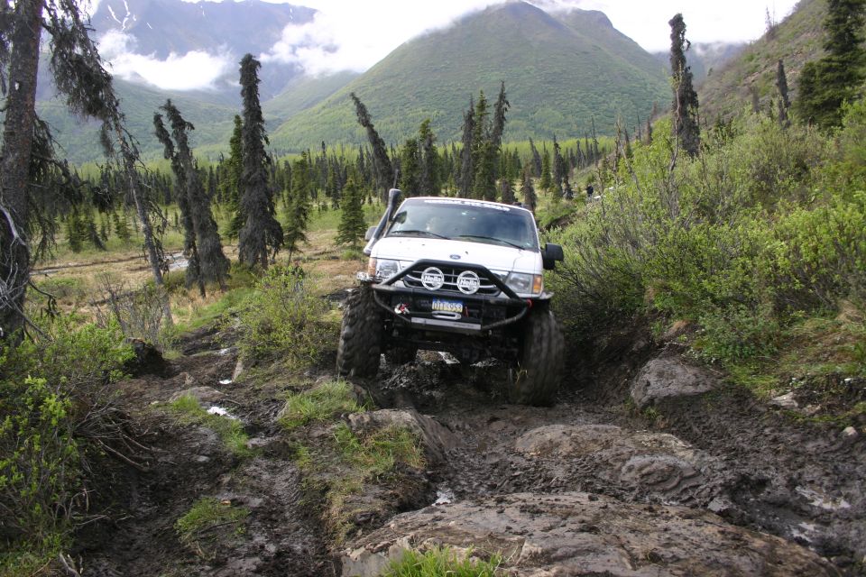 White off-road vehicle navigating a muddy, rocky trail with snorkel and winch