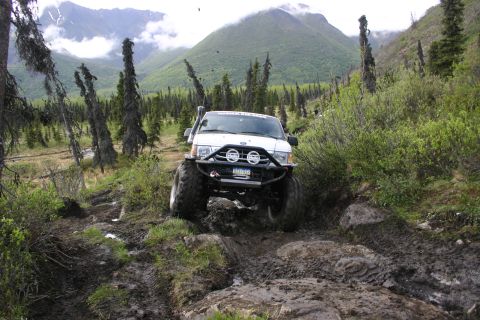 2003 Jeep TJ - Off-road SUV tackling a challenging muddy and rocky path in a mountainous, wooded area.