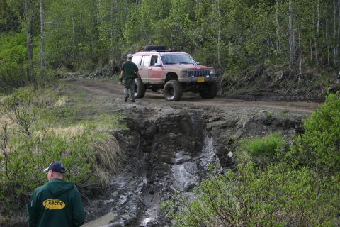 2003 Jeep TJ - A modified Jeep Cherokee XJ navigates a challenging, eroded dirt path surrounded by dense forest.
