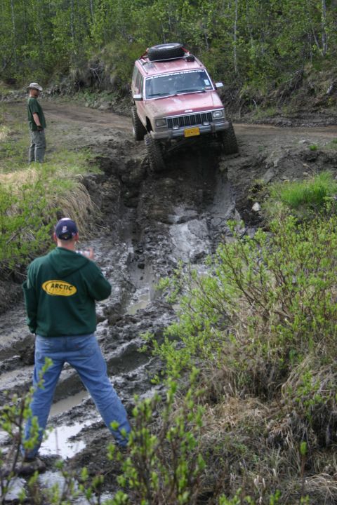 2003 Jeep TJ - A red Jeep Cherokee XJ tackles a challenging muddy incline during an off-road event.