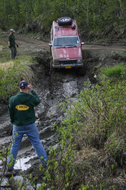 2003 Jeep TJ - Jeep Cherokee XJ attempts to climb a steep, muddy incline with a photographer capturing the moment.