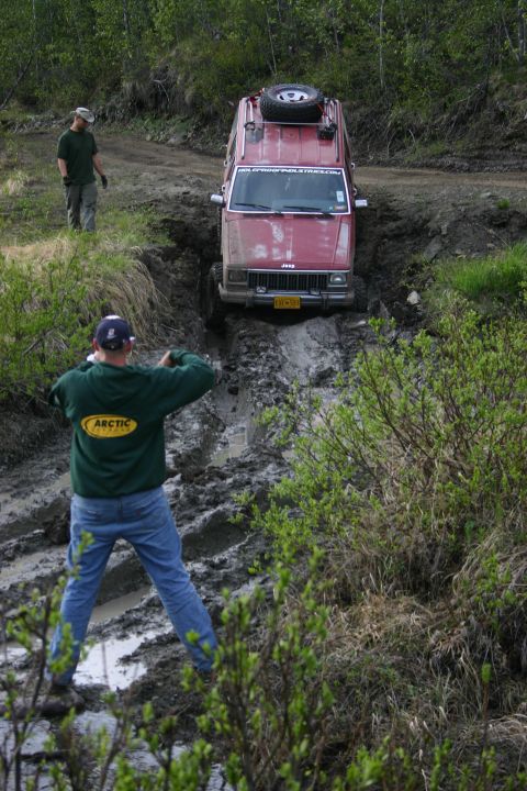 2003 Jeep TJ - A red Jeep Cherokee navigates a muddy trail while a person films the action.