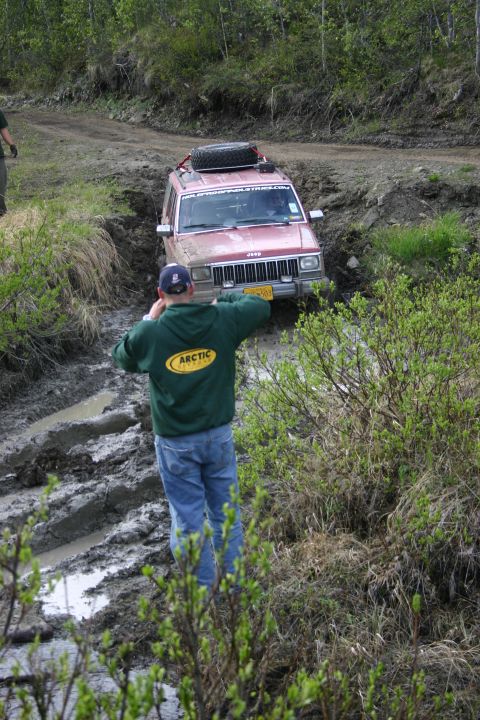 2003 Jeep TJ - A red Jeep Cherokee XJ navigates a muddy trail, with a person watching from the side.