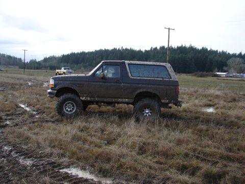 1996 Ford Bronco - This lifted 1996 Ford Bronco navigates a challenging muddy terrain, with another vehicle visible in the background.