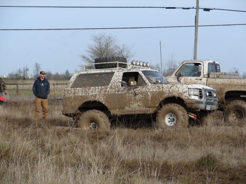 1996 Ford Bronco - Two off-road vehicles covered in mud, parked in a grassy field with a man standing nearby.