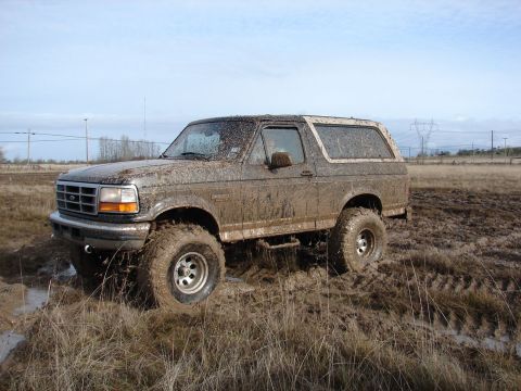 1996 Ford Bronco - A muddy 1996 Ford Bronco navigates a challenging off-road terrain.
