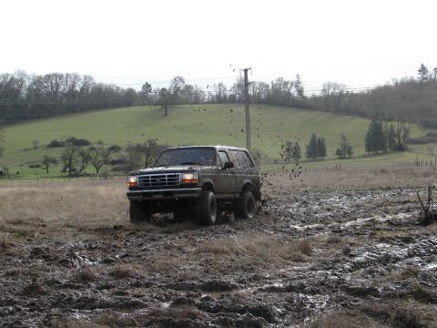 1996 Ford Bronco - A 1996 Ford Bronco navigates a challenging muddy terrain, with mud flying from its tires.