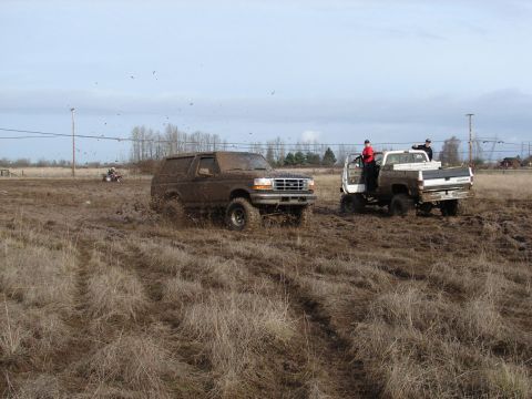 1996 Ford Bronco - Two vehicles are stuck in a muddy field, with one ATV in the background.
