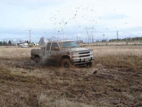 1996 Ford Bronco - Pickup truck stuck in mud, splashing dirt everywhere.