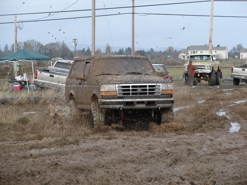 1996 Ford Bronco covered in mud, driving through a muddy field