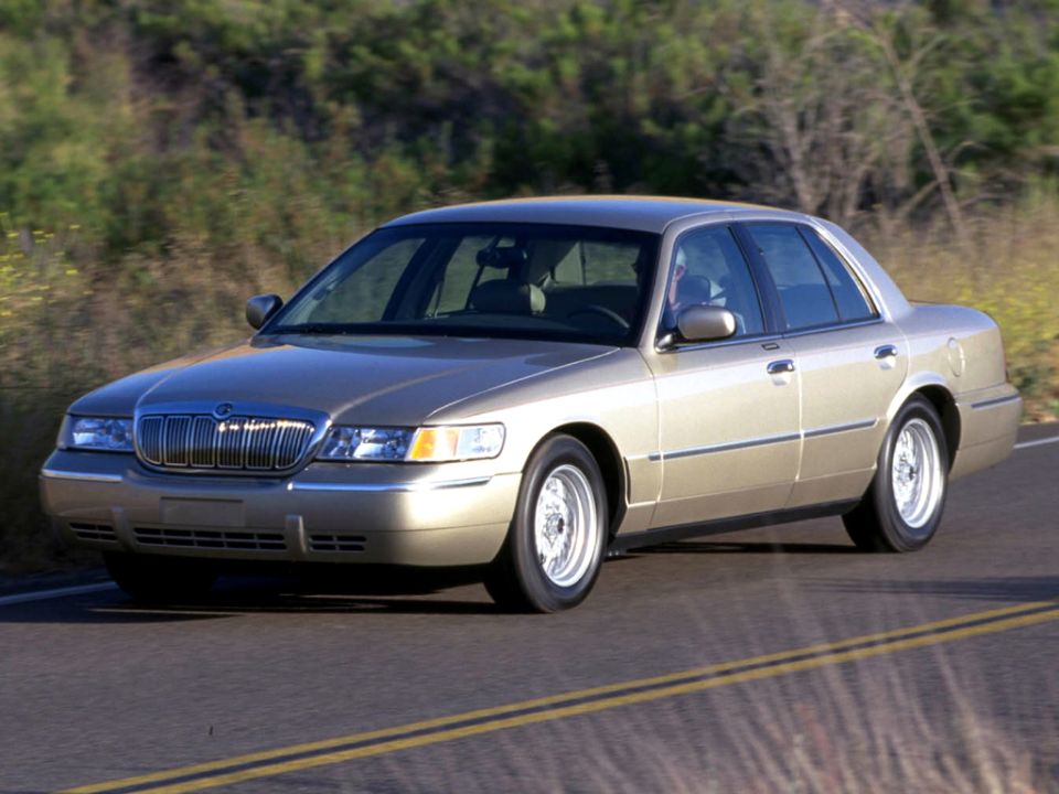 Tan Mercury Grand Marquis sedan front three-quarter on a curving road through dry brush