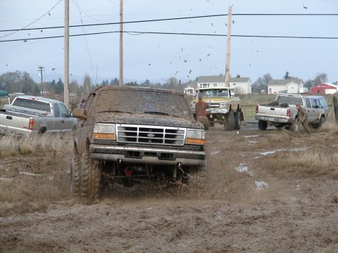 1996 Ford Bronco - Several trucks, including a 1996 Ford Bronco, are stuck in deep mud during an off-road event.