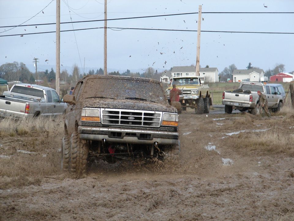 1996 Ford Bronco driving through mud with other trucks in background